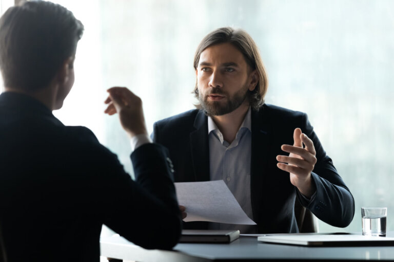 Serious young executive manager with long hairstyle in formal suit discussing business agreement details with focused male partner at negotiation meeting, hr holding job interview with candidate.