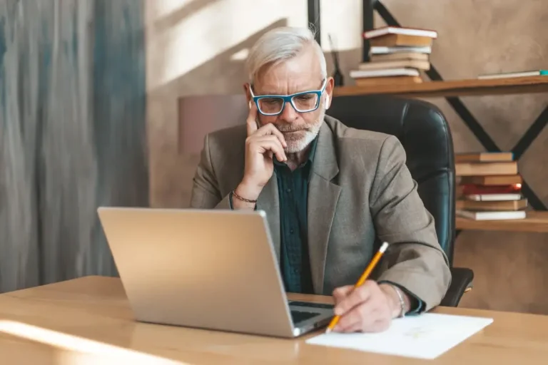 Signing testament. Senior man at the table writes on paper. Financial difficulties.